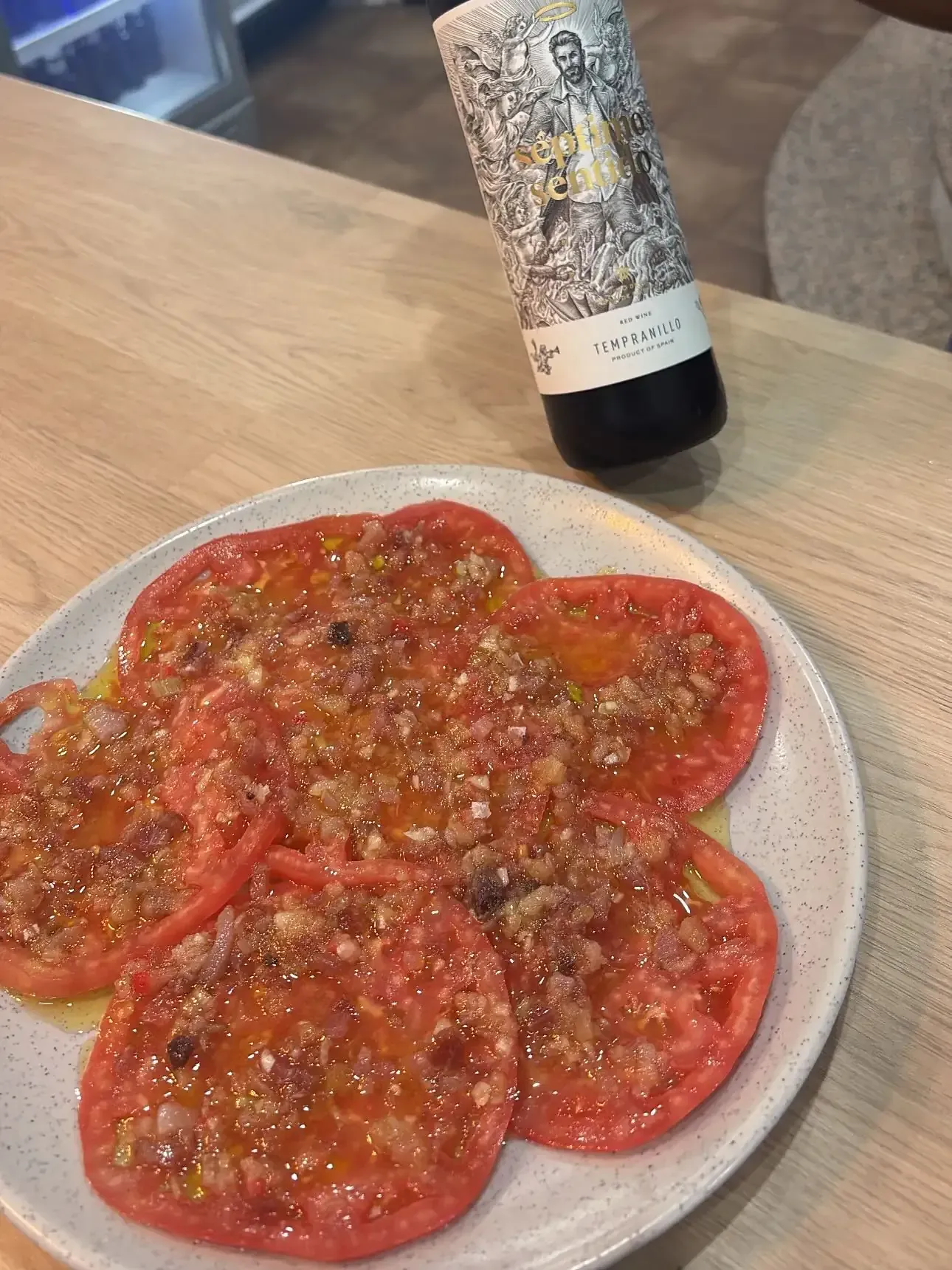 Tomates en rodajas en un plato cubiertos con aderezo, con una botella de vino.