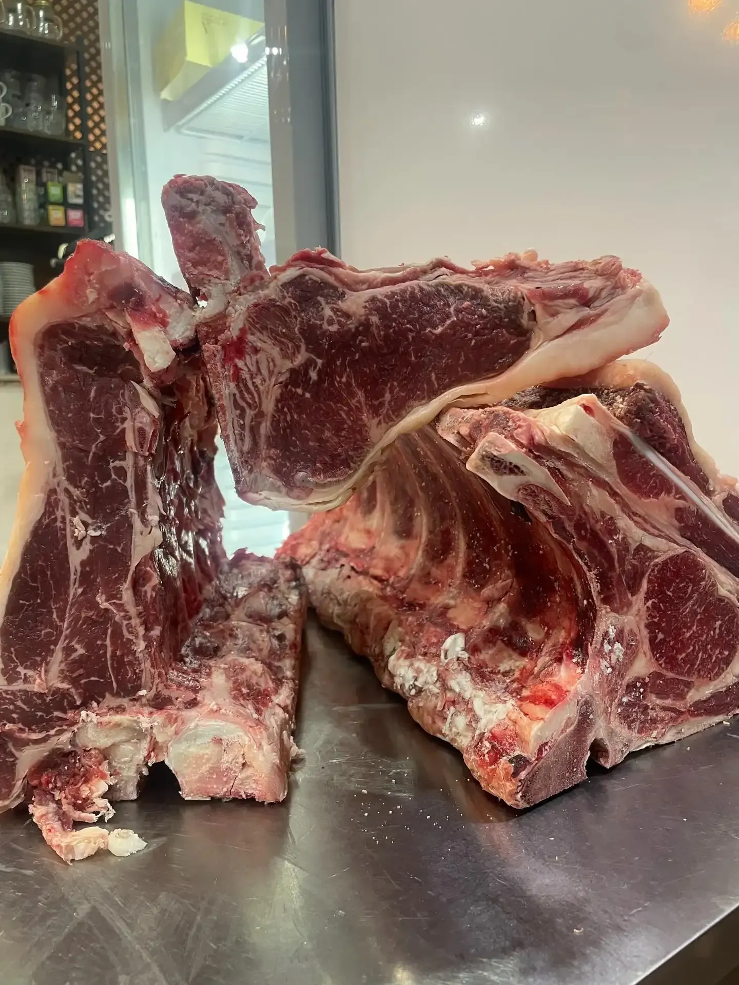 Filetes T-bone crudos, cortados en trozos gruesos, apilados sobre una superficie metálica, listos para cocinar.