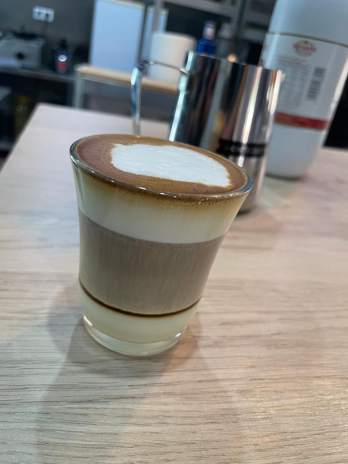 Una bebida de café en capas en un vaso transparente sobre una superficie de madera.