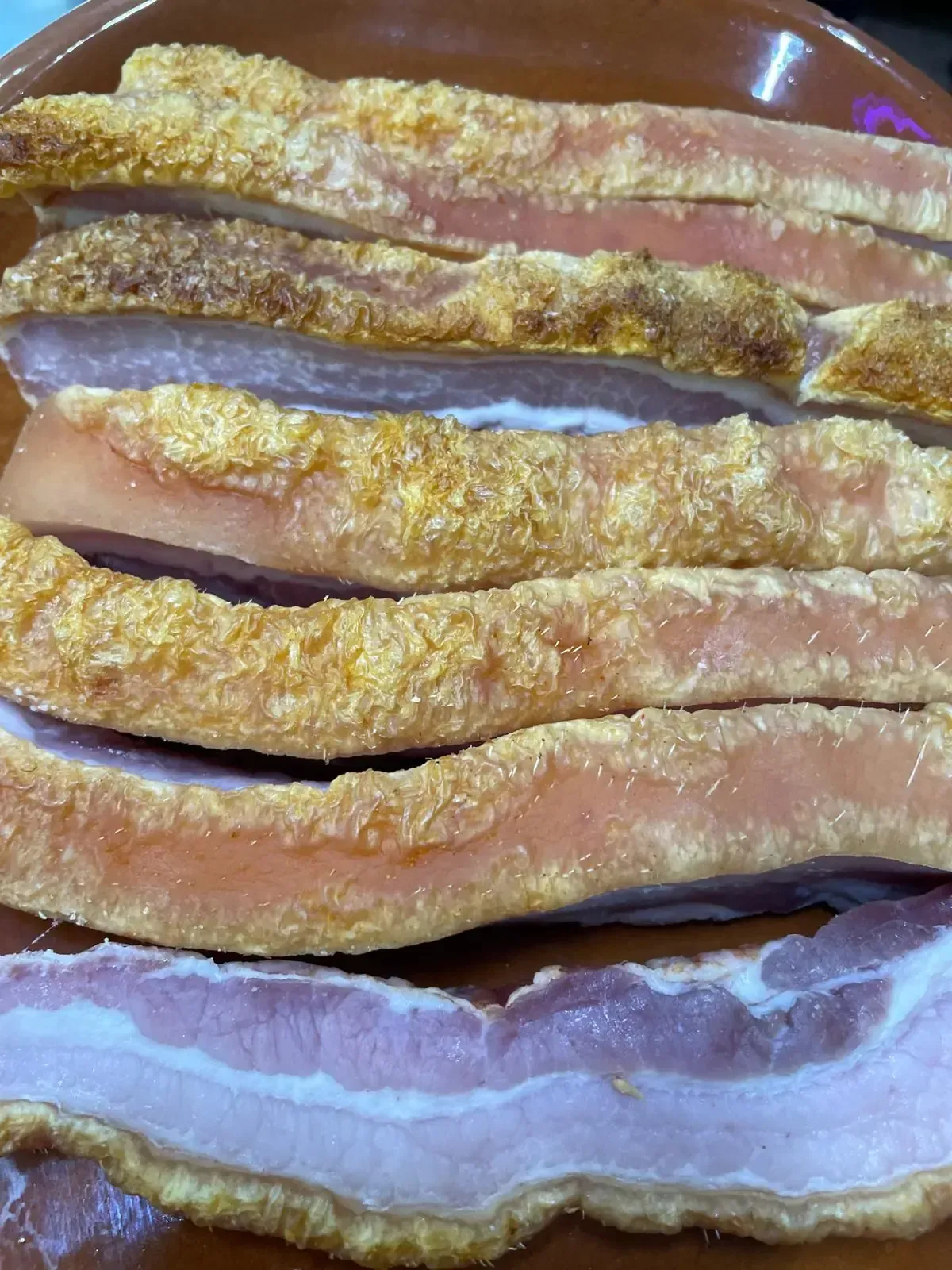 Rebanadas de panceta de cerdo crujiente con chicharrón, servidas en una fuente marrón.