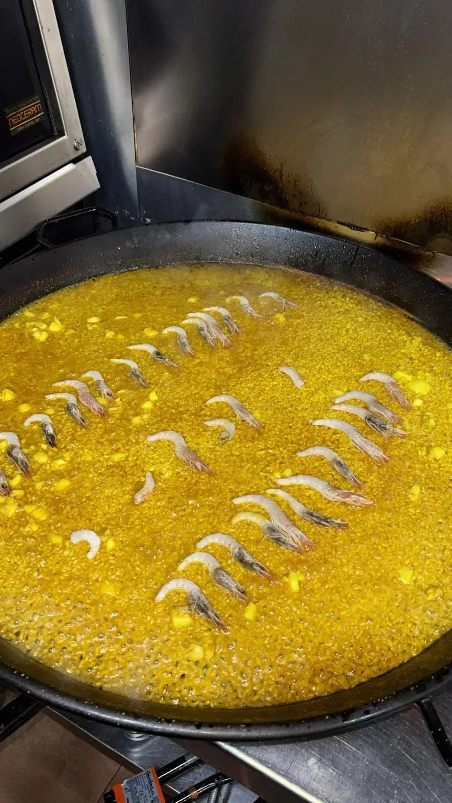 Paella cocinándose en una sartén grande y redonda con caldo amarillo y camarones dispuestos en filas.