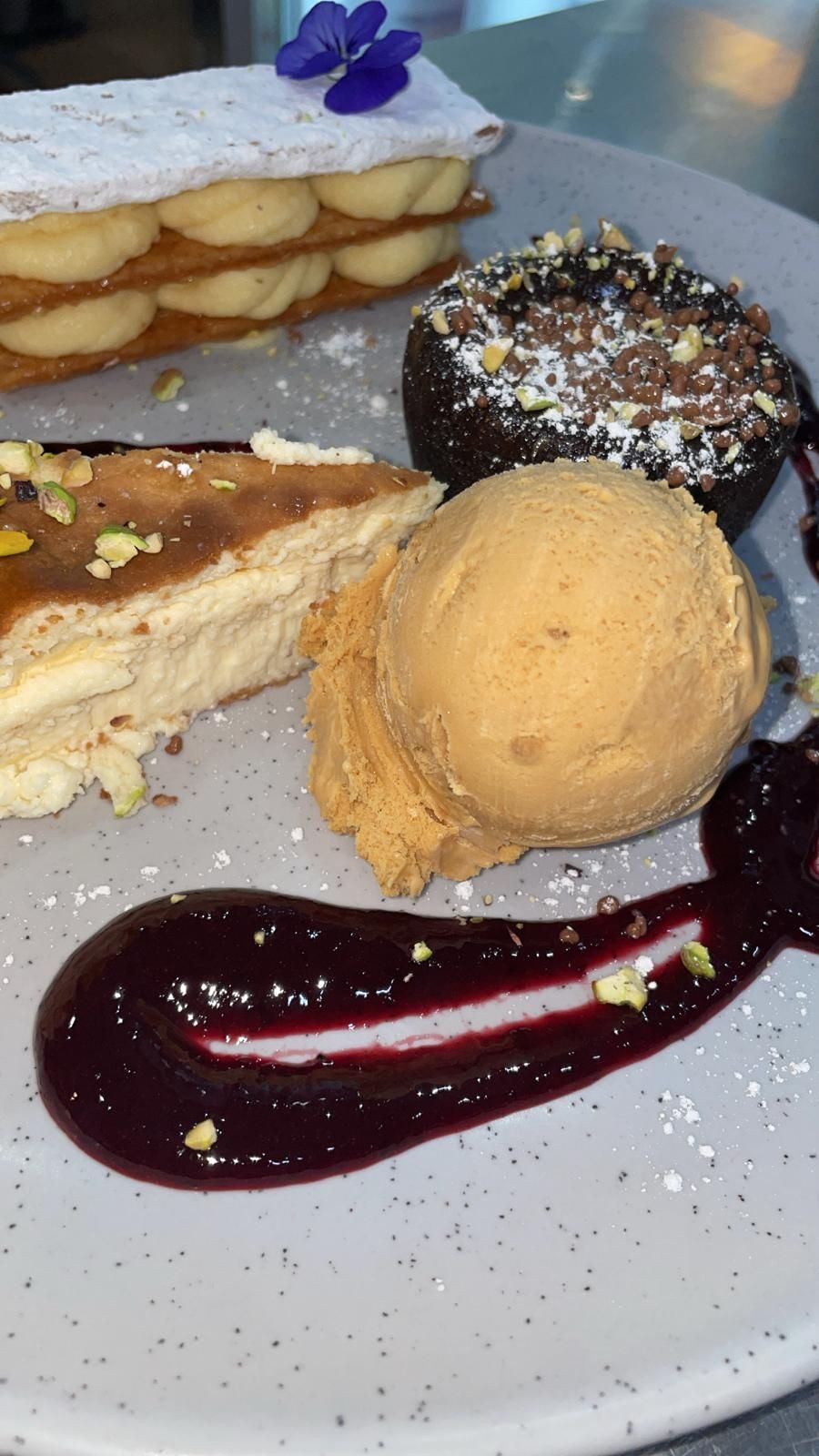 Plato de postre: milhojas, tarta de chocolate, helado, tarta de queso, salsa de frutos rojos y pistachos.