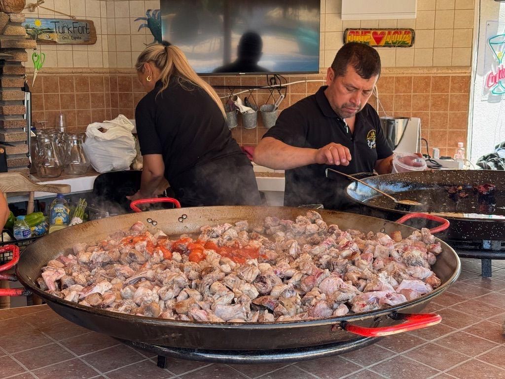 Dos personas cocinando un plato grande en una sartén gigante al aire libre.