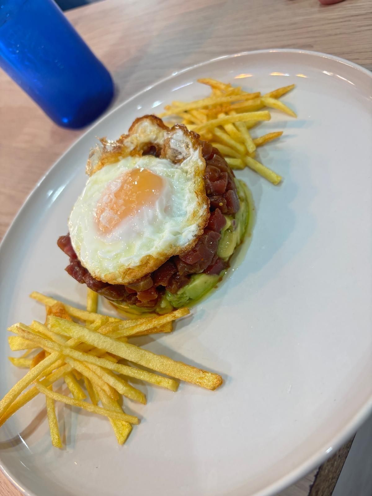 Plato con aguacate, tartar de ternera, huevo frito y patatas fritas en plato blanco.
