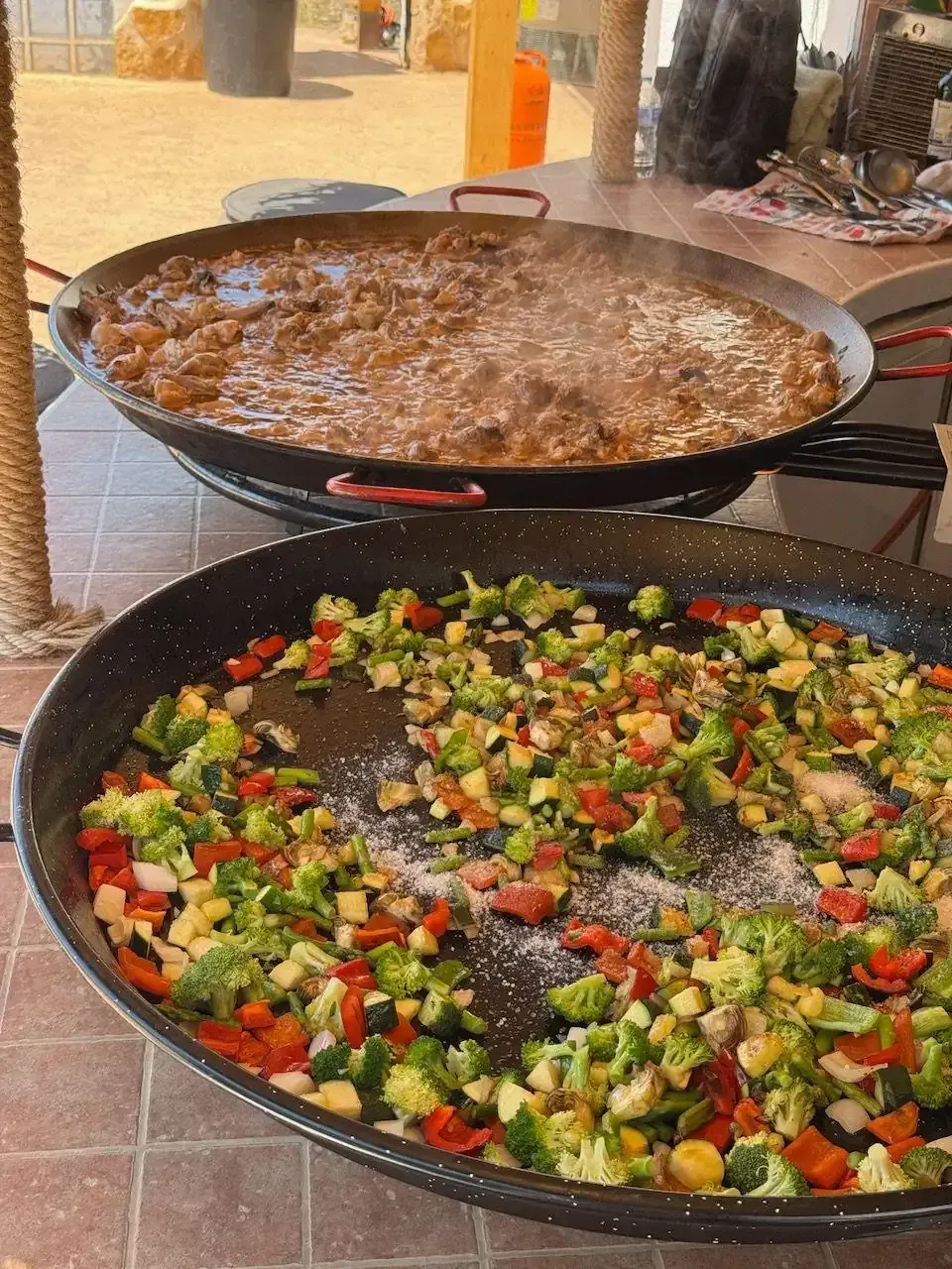 Dos grandes ollas de comida. Una con verduras y la otra con una sustancia oscura parecida a un guiso, al aire libre.