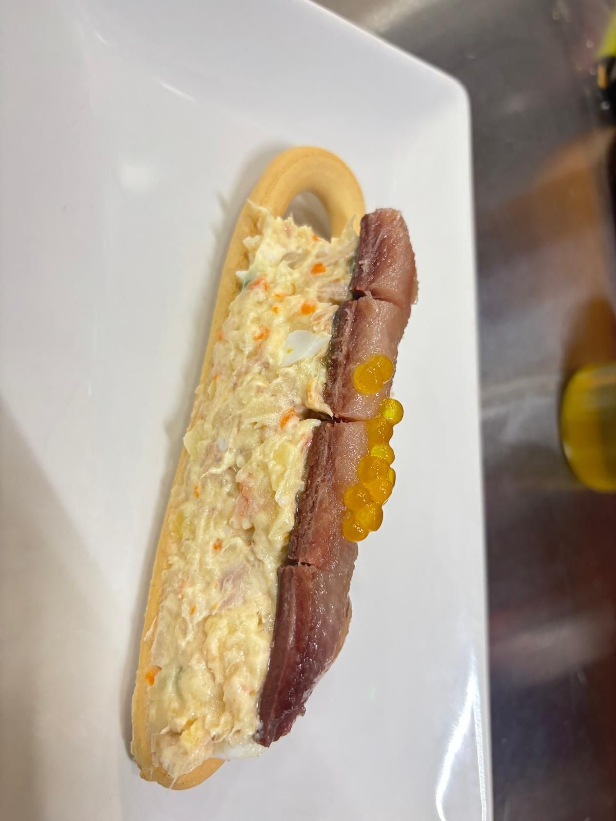 Tapas con galleta: ensalada cremosa y pescado curado con huevas de naranja. Plato blanco.