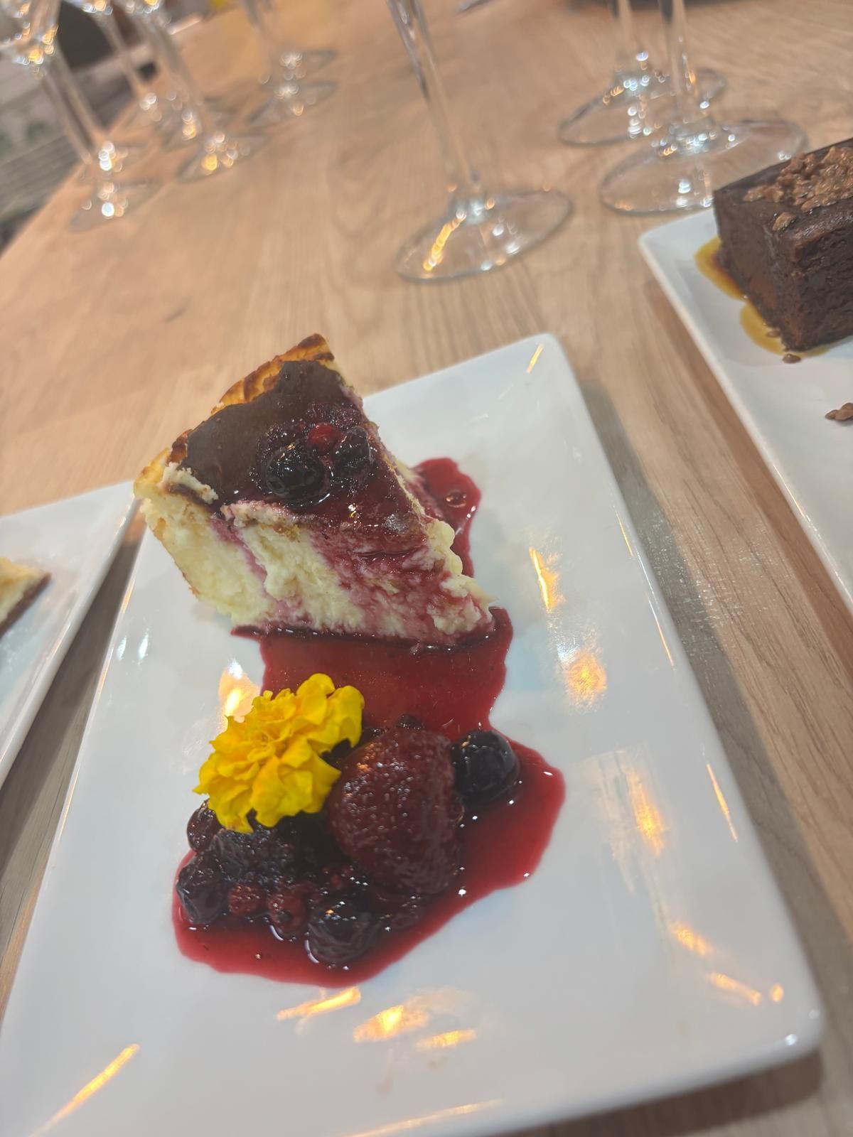 Rebanada de tarta de queso con compota de bayas y flores comestibles en un plato blanco.