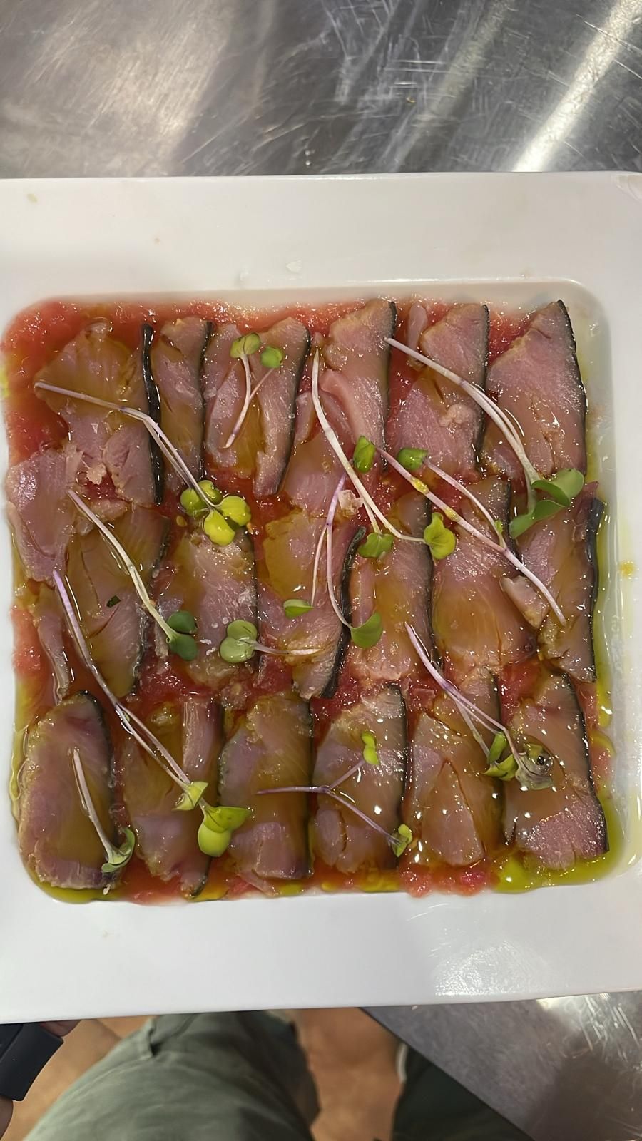 Carne cortada finamente en un plato blanco, rociada con salsa y adornada con brotes.