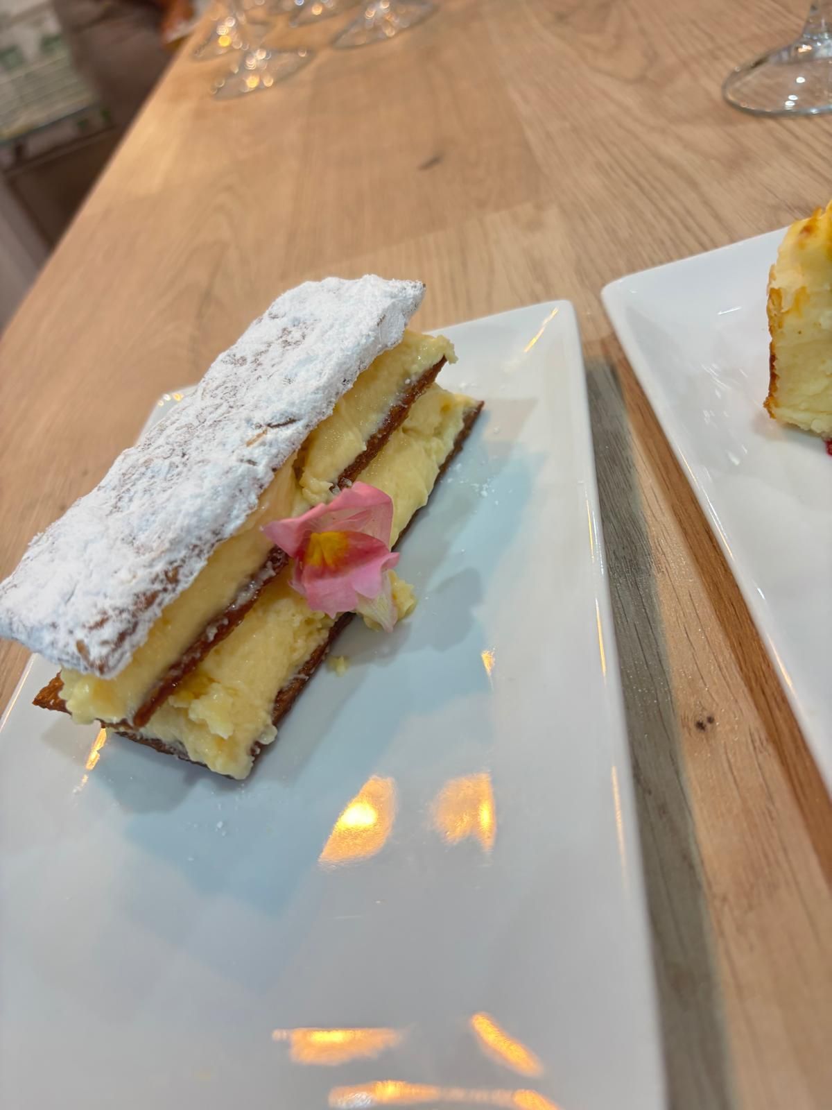 Postre de hojaldre con capas de crema, decorado con una flor y azúcar glas, sobre un plato blanco.