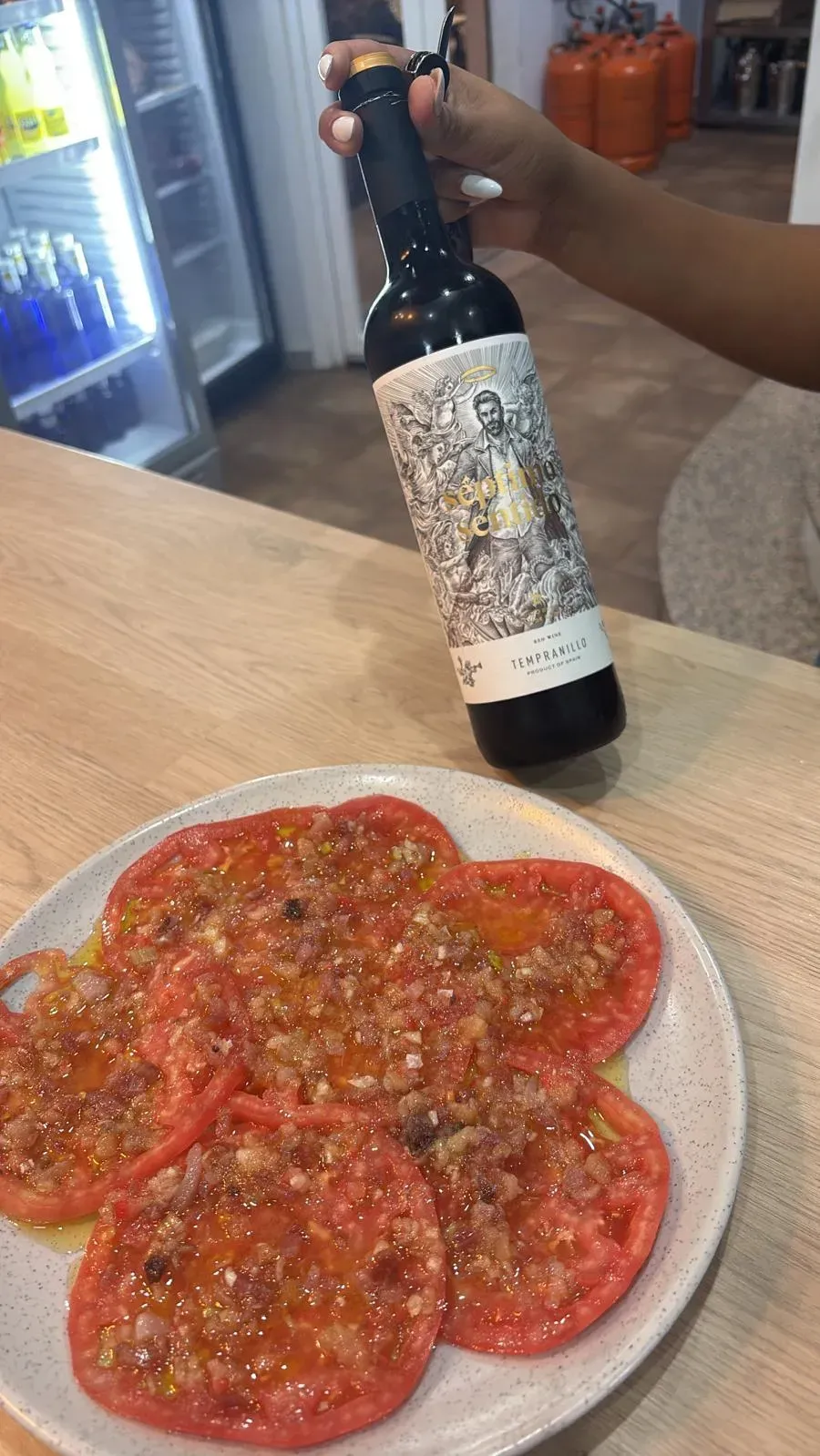 Plato de tomates en rodajas con aderezo junto a una botella en mano.