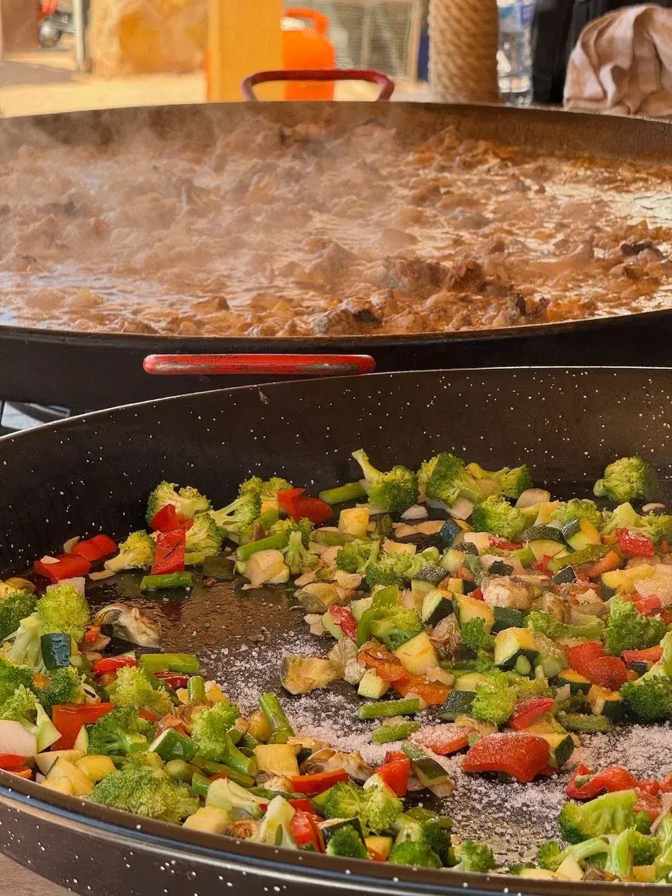 Grandes ollas de comida cocinándose al aire libre: una con verduras, otra con un guiso de carne.