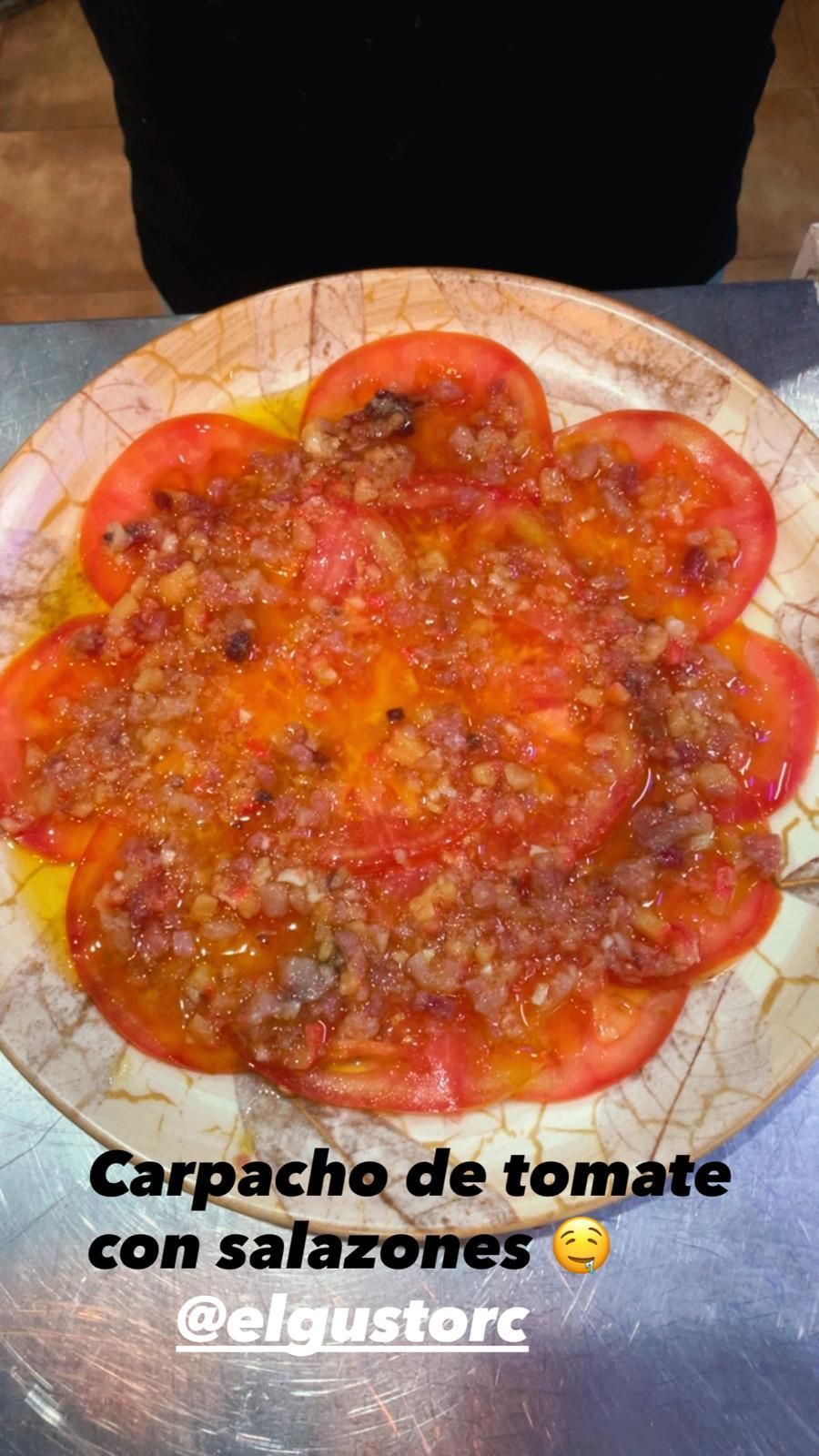 Carpaccio de tomate con pescado salado en plato decorativo.