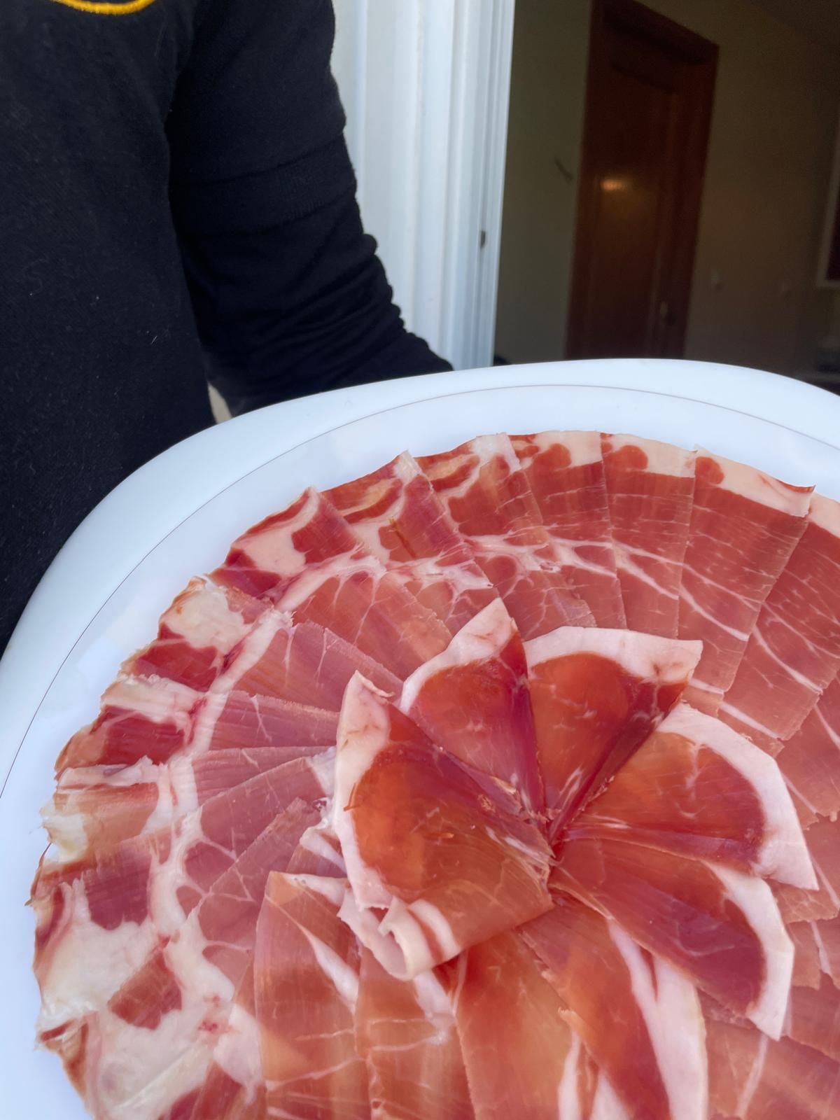 Persona sosteniendo un plato blanco de jamón curado cortado fino.