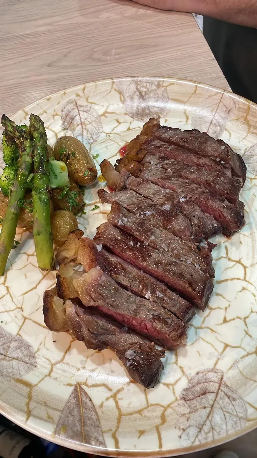 Filete en rodajas, espárragos y patatas en un plato con diseño de hojas.