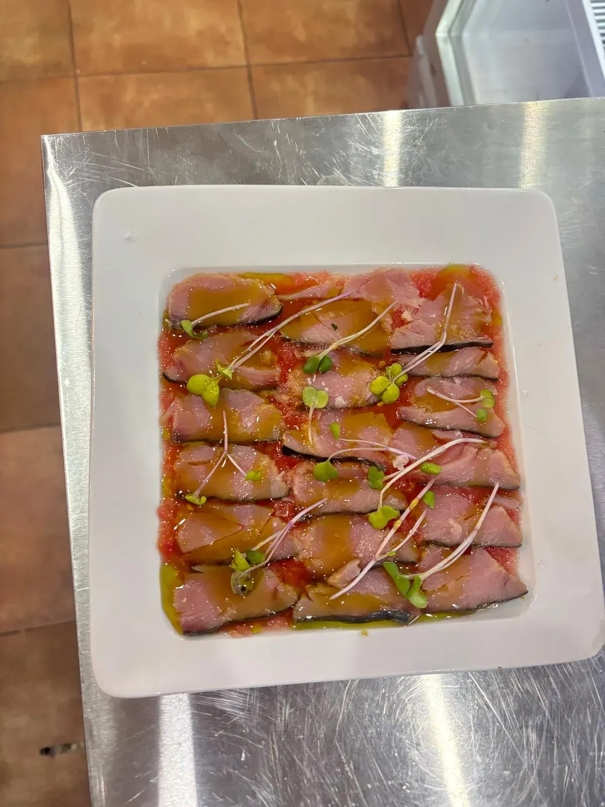 Plato de carne cortada finamente en salsa de tomate, adornado con brotes, en un plato blanco.