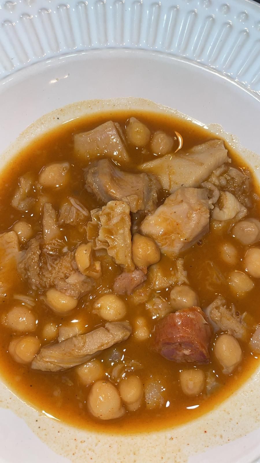 Un plato de guiso con garbanzos, carne y chorizo en un rico caldo de color naranja.