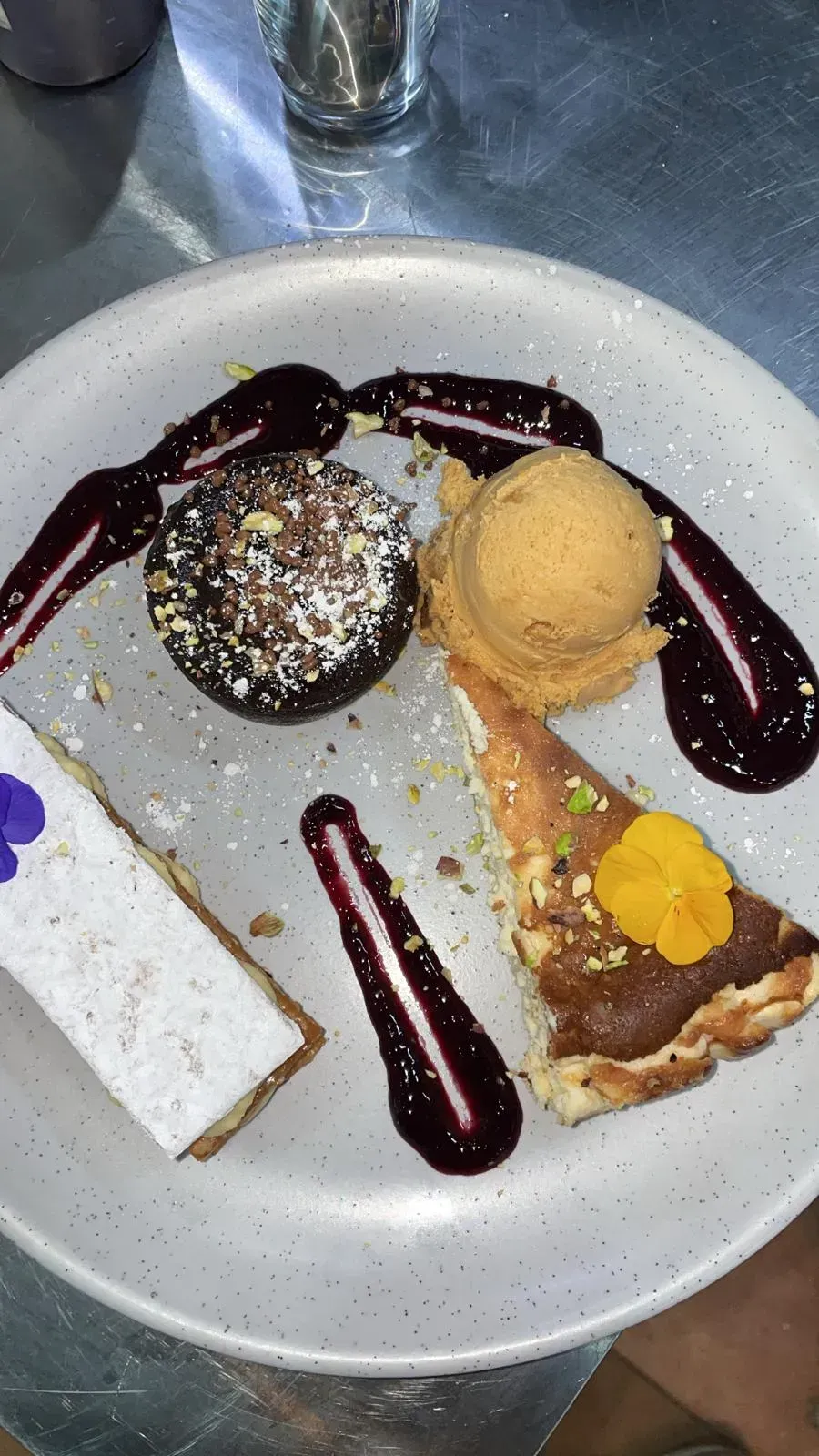 Plato de postre con tarta de chocolate, tarta, helado y salsa de frutos rojos.