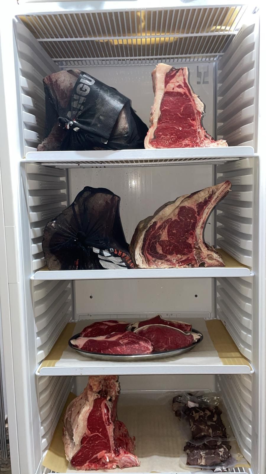 Vitrina refrigerada con varios filetes crudos madurados en seco en estantes, que muestran diferentes cortes y etapas de maduración.