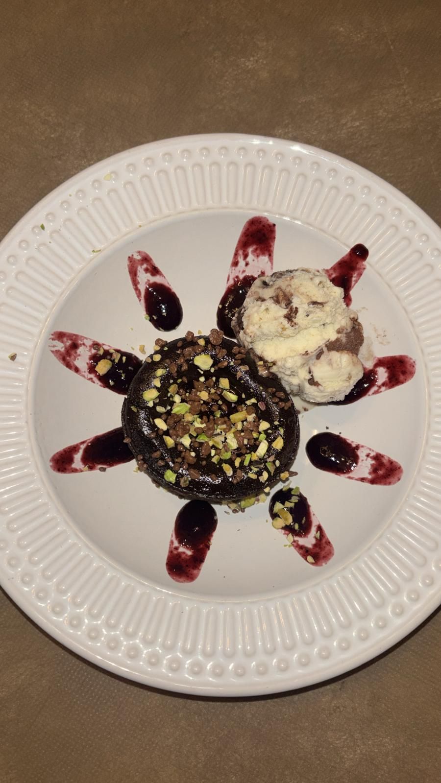 Postre de chocolate con helado, salsa de frutos rojos y pistachos en un plato blanco.