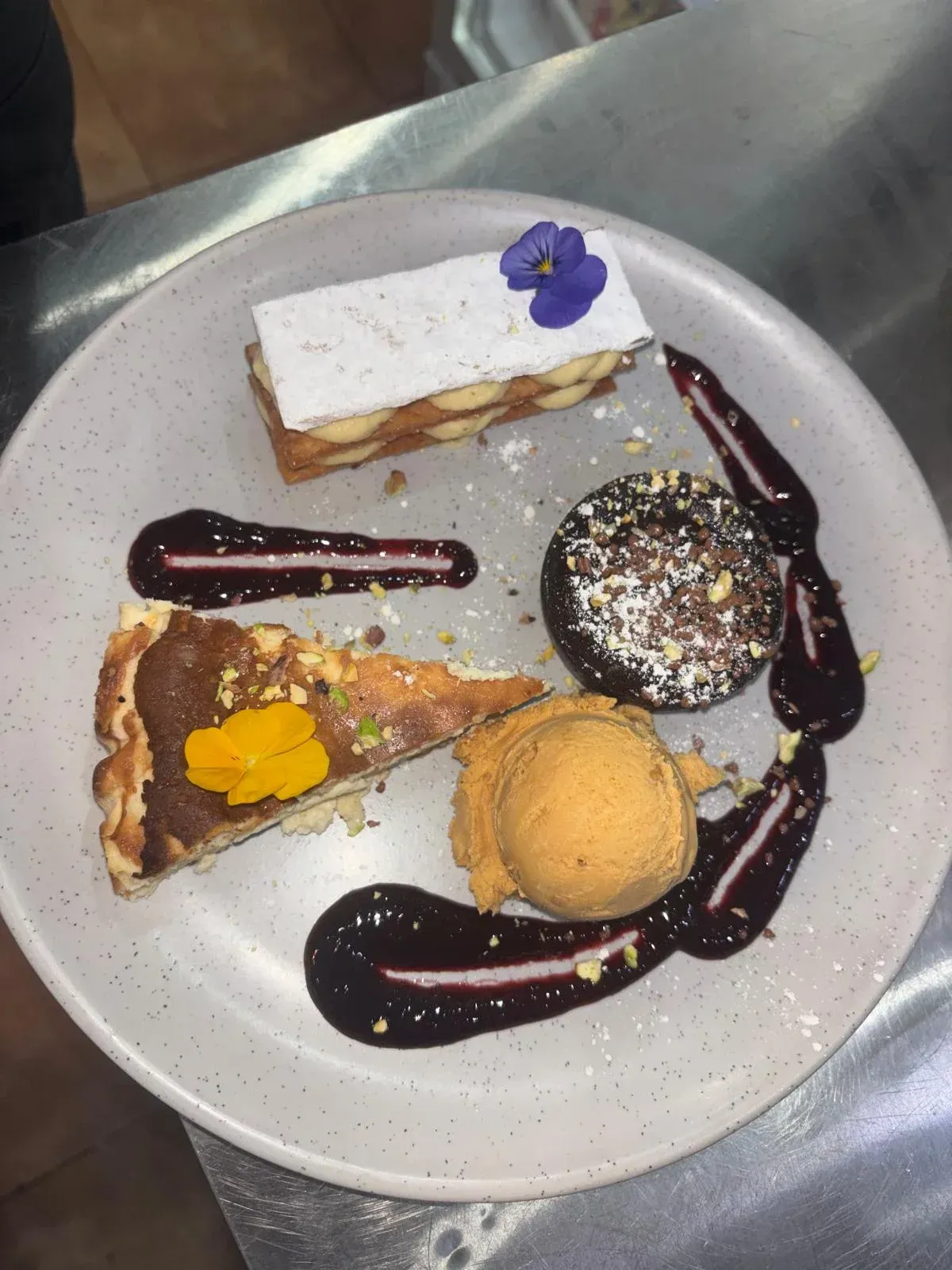 Plato de postre con masa de hojaldre, bizcocho de chocolate, helado y tarta, todo ello bañado en salsa.