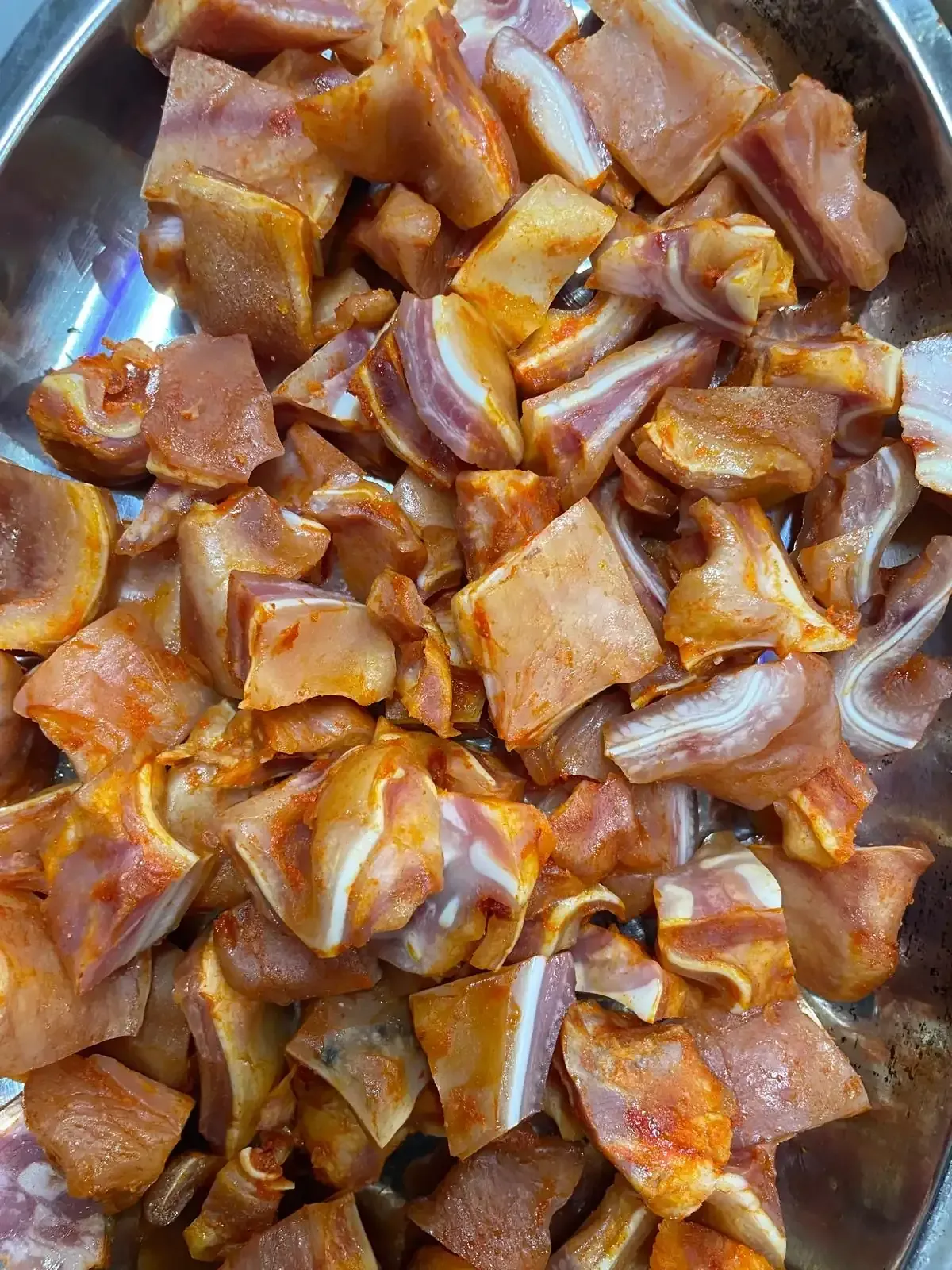 Orejas de cerdo picadas y sazonadas en un recipiente de metal, listas para cocinar.