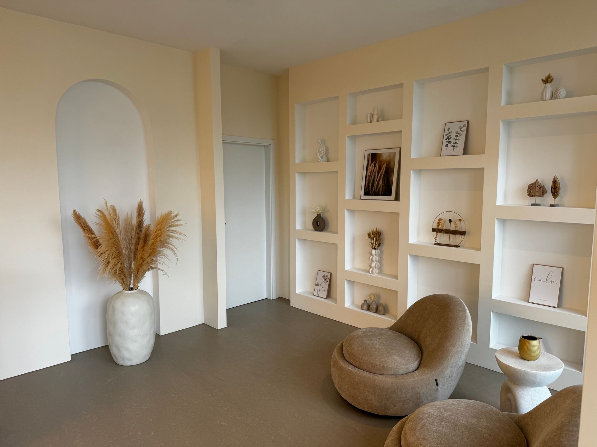 Ein helles Zimmer mit zwei Stühlen und einer Vase mit getrocknetem Gras an der Wand.