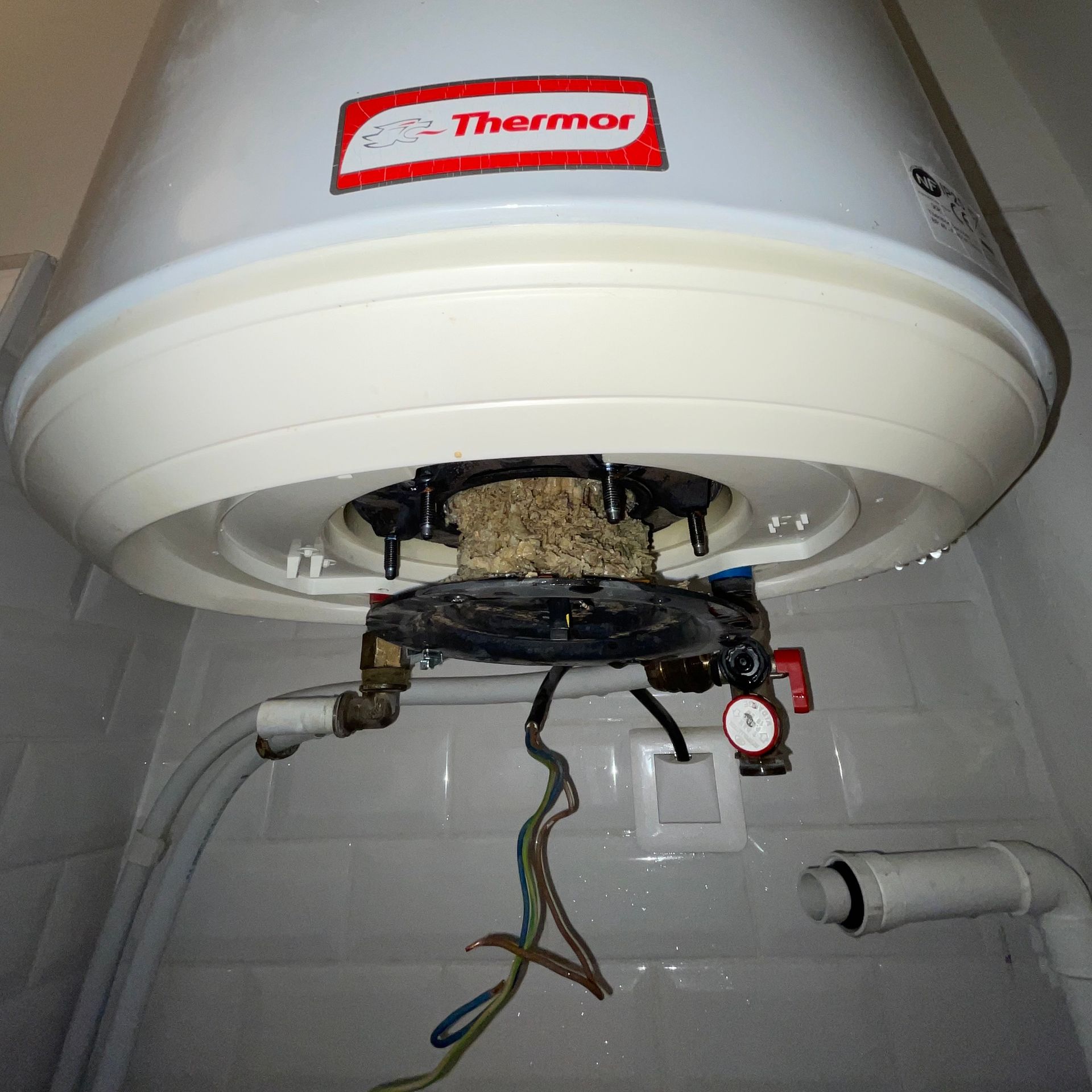 Un plombier de dos sous un ballon d'eau chaude accroché au mur d'une salle de bain