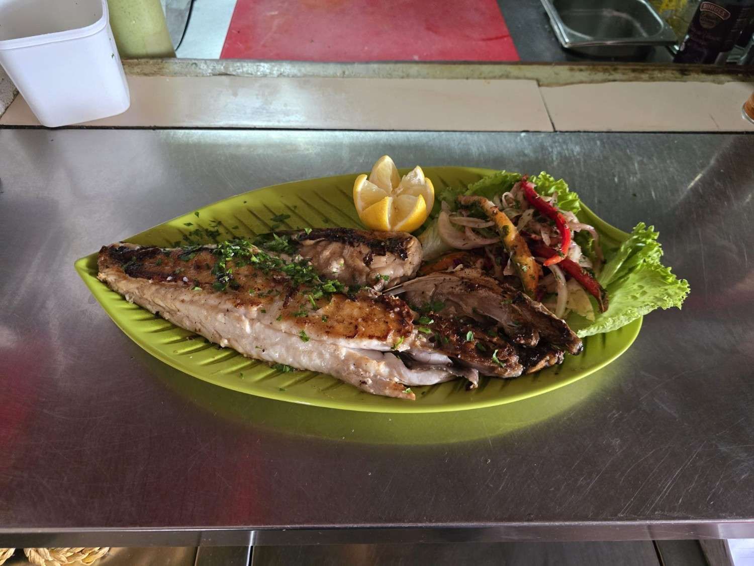 Plato de pescado a la plancha con verduras, limón y una copa de vino blanco.
