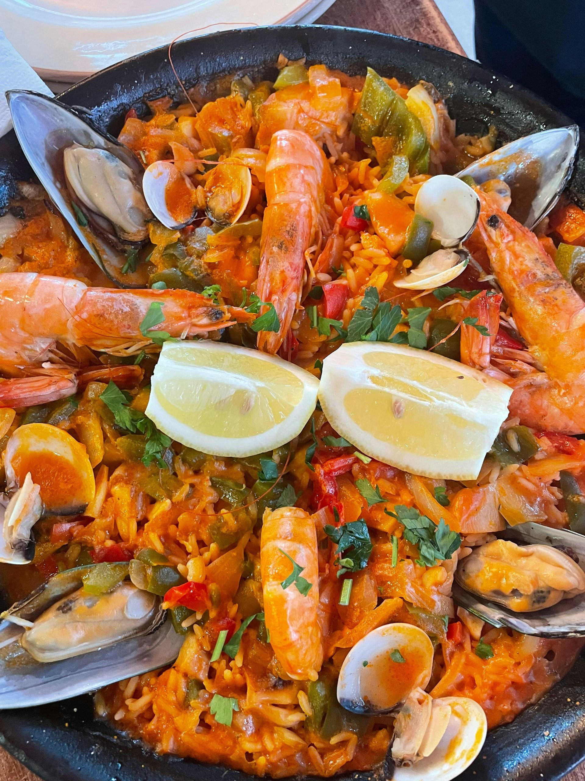 Paella de mariscos en sartén negra, con camarones, mejillones, almejas, arroz y rodajas de limón.