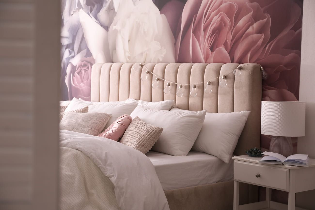 Un dormitorio con una cama, mesita de noche, lámpara y un mural en la pared.