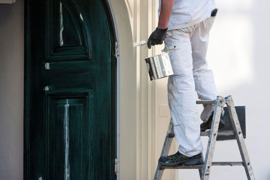 Un hombre está de pie en una escalera pintando una puerta.