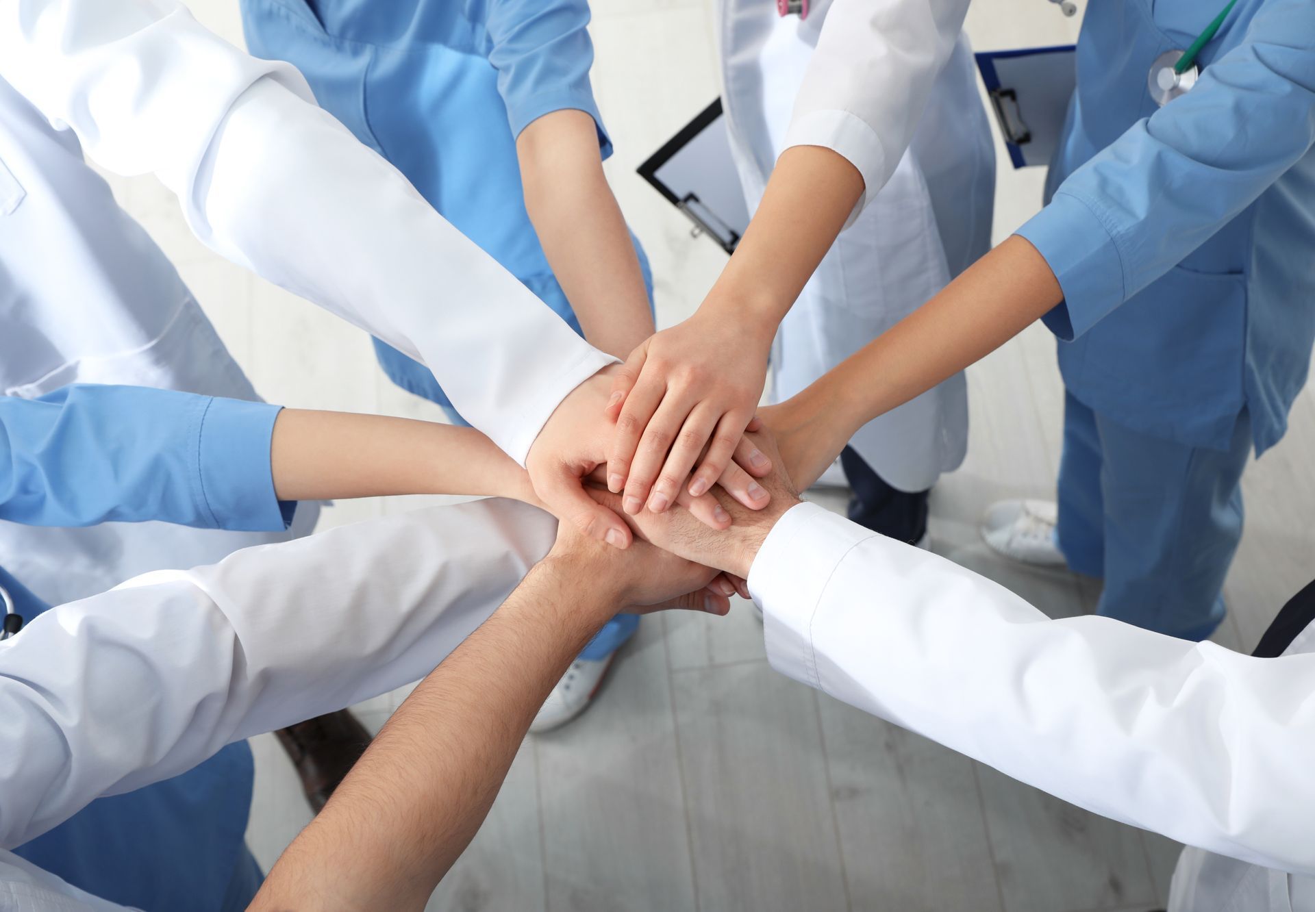 Eine Gruppe von Ärzten und Krankenschwestern legt ihre Hände zu einem Kreis zusammen.