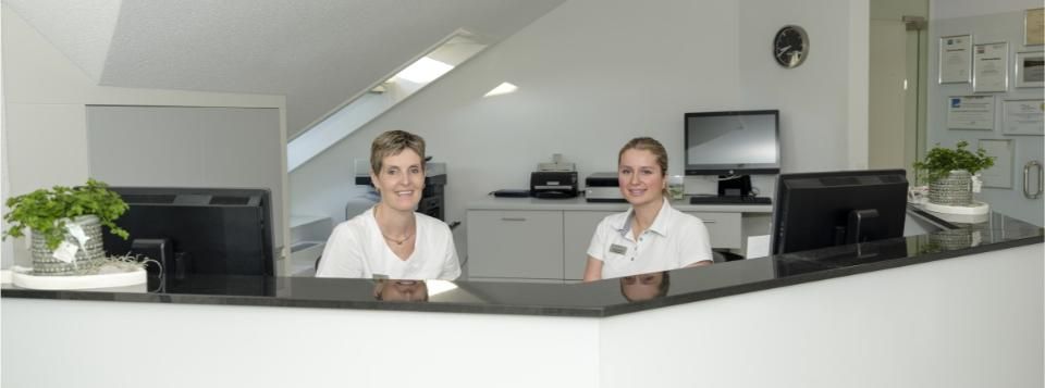 Zwei Assistentinnen sitzen am Tresenvon der Praxis Walter A. Aeschbacher
