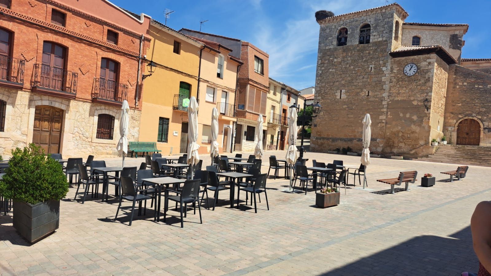 Una plaza de la ciudad con mesas y sillas y una torre de reloj al fondo.