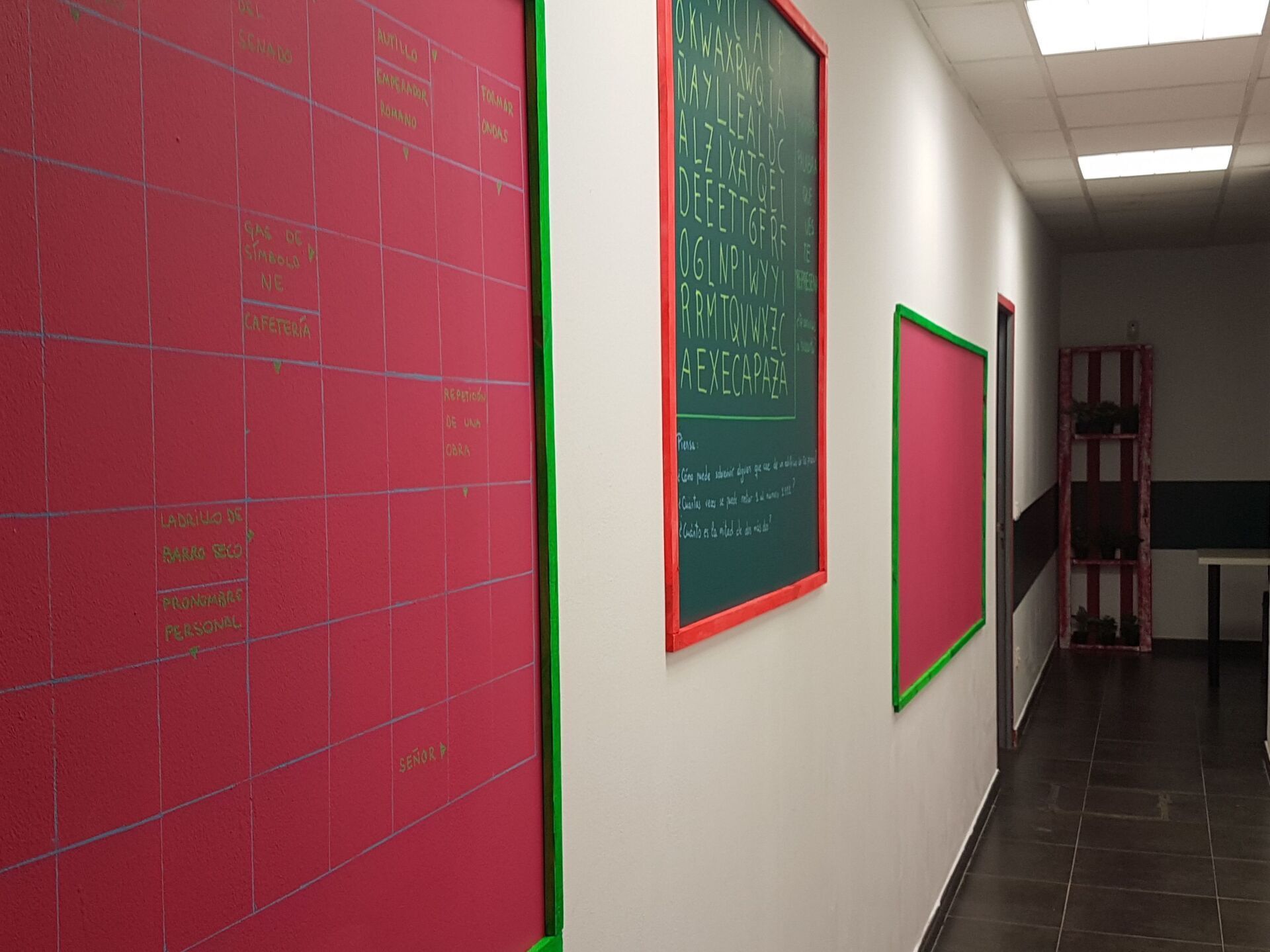Un pasillo con tableros con marcos rojos y verdes sobre paredes blancas. Una puerta al final del pasillo.