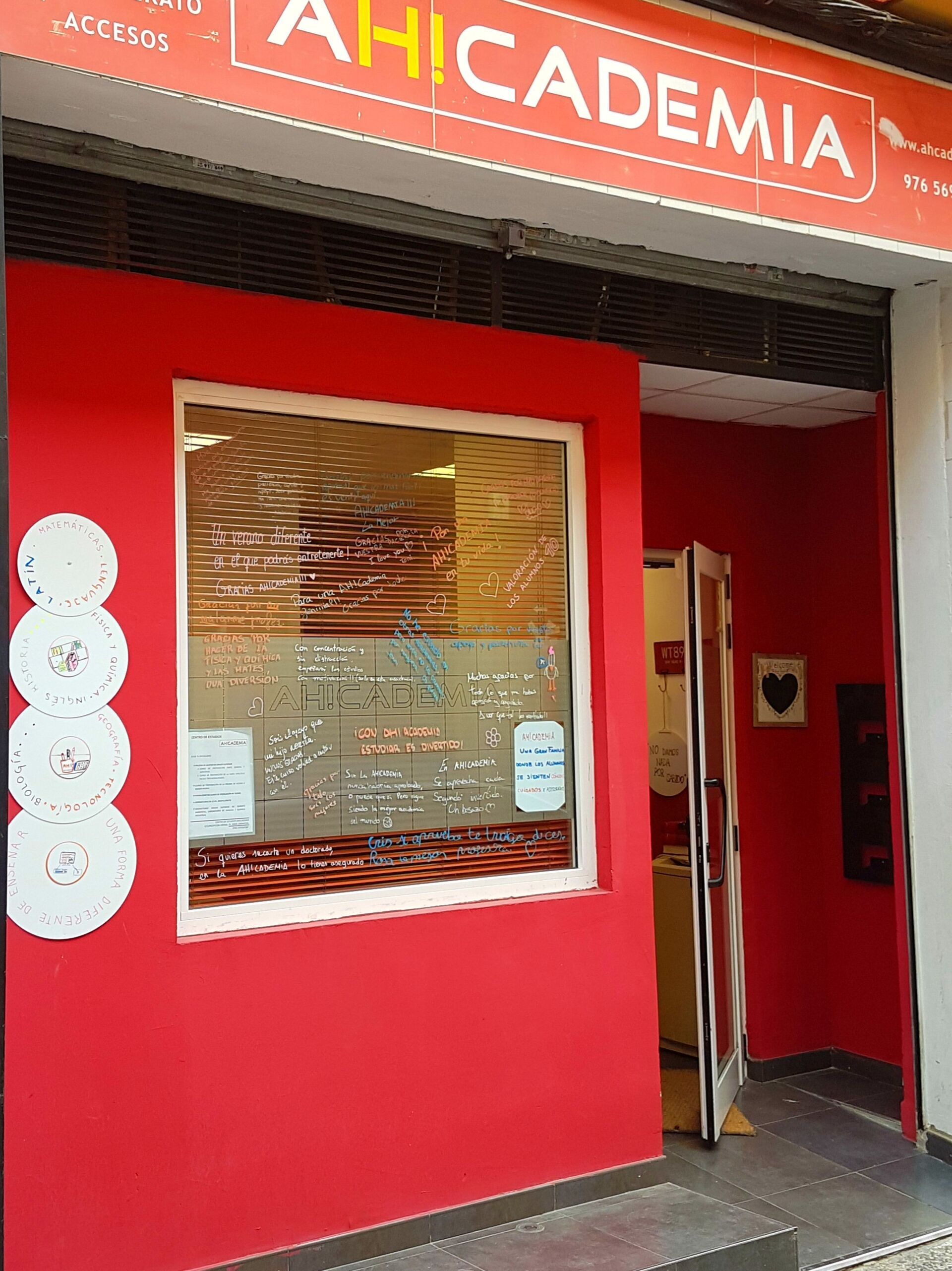 Fachada roja de Ahicademia con puerta y ventana abiertas.