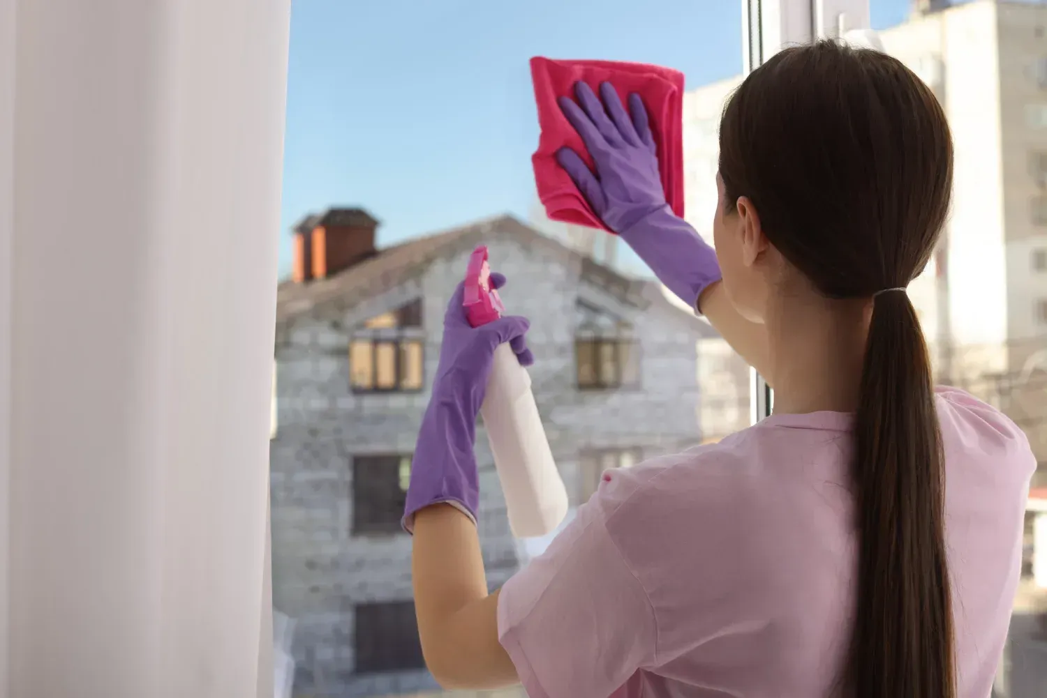 Una mujer está limpiando una ventana con un paño y spray.