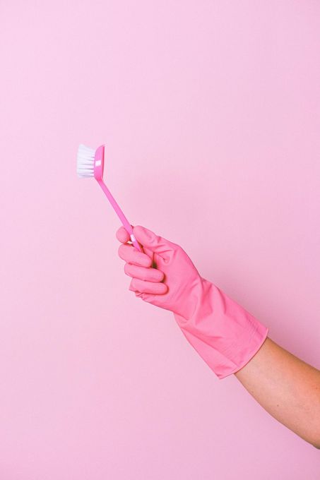 Una mano en un guante de goma rosa sostiene un cepillo de dientes rosa.