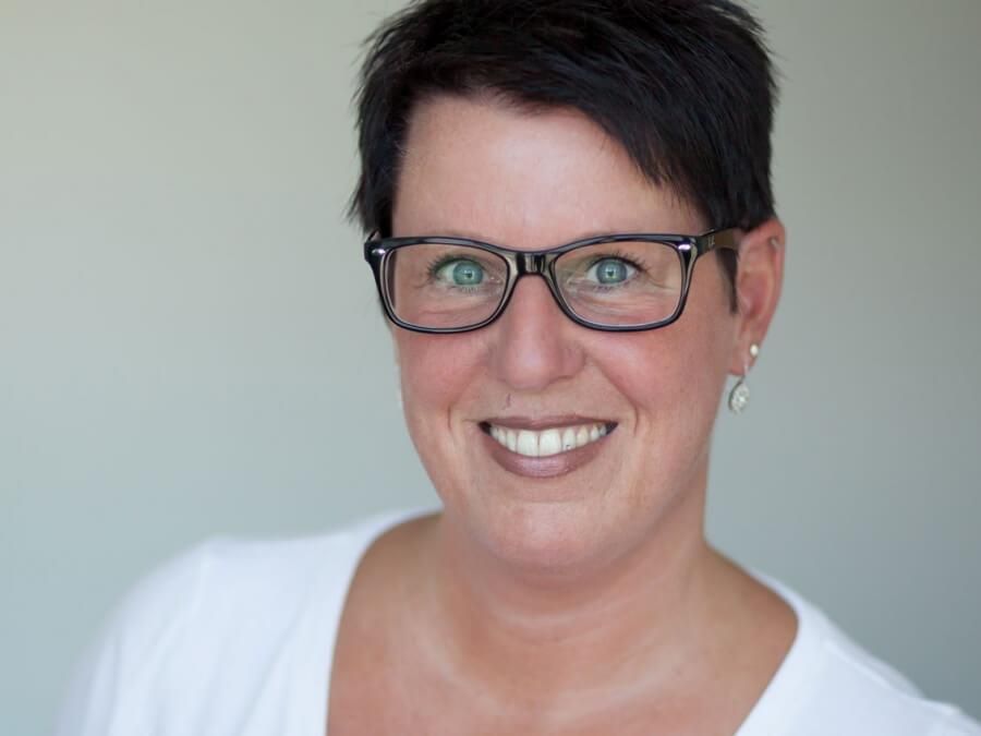 Eine Frau mit Brille und weißem Hemd lächelt in die Kamera