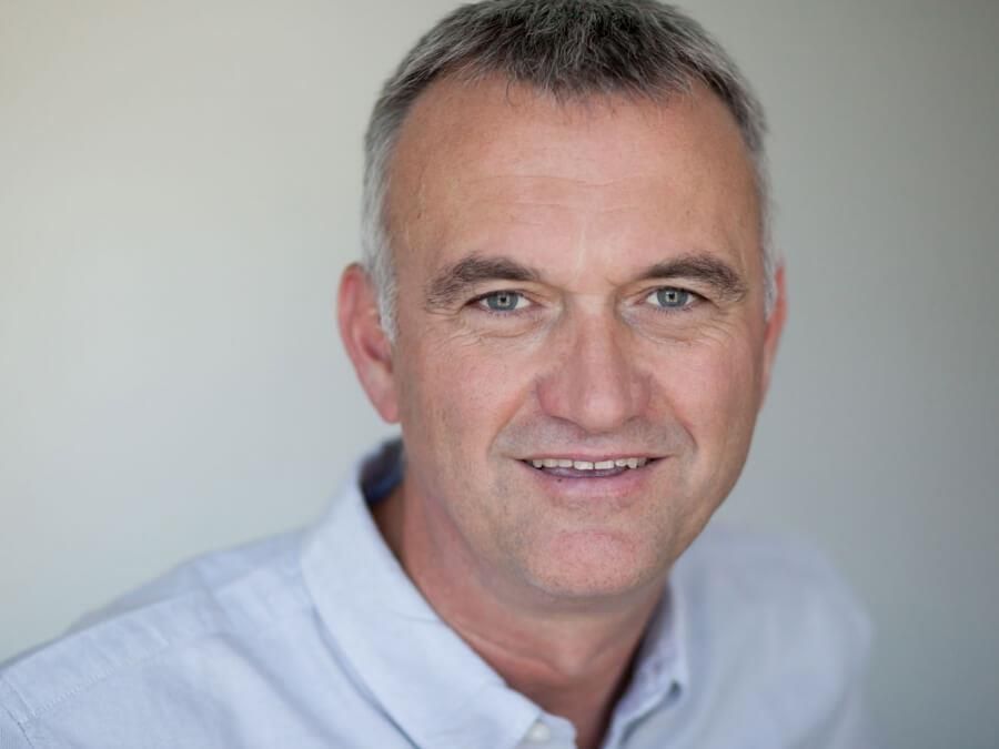 Ein Mann im weißen Hemd lächelt in die Kamera.