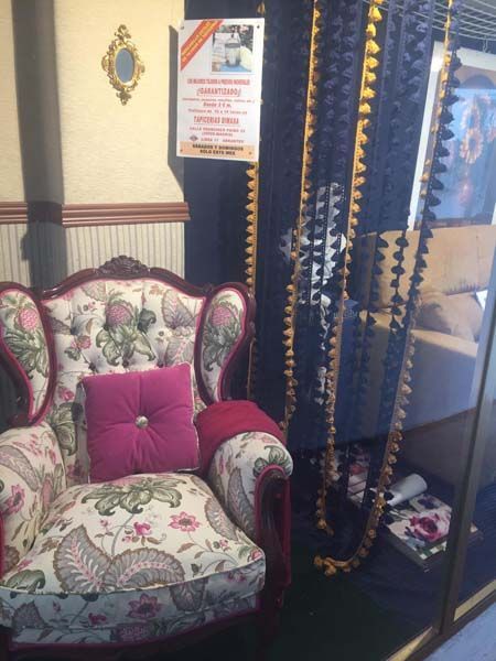 Sillón floral con almohada rosa; cortina decorativa; póster enmarcado.