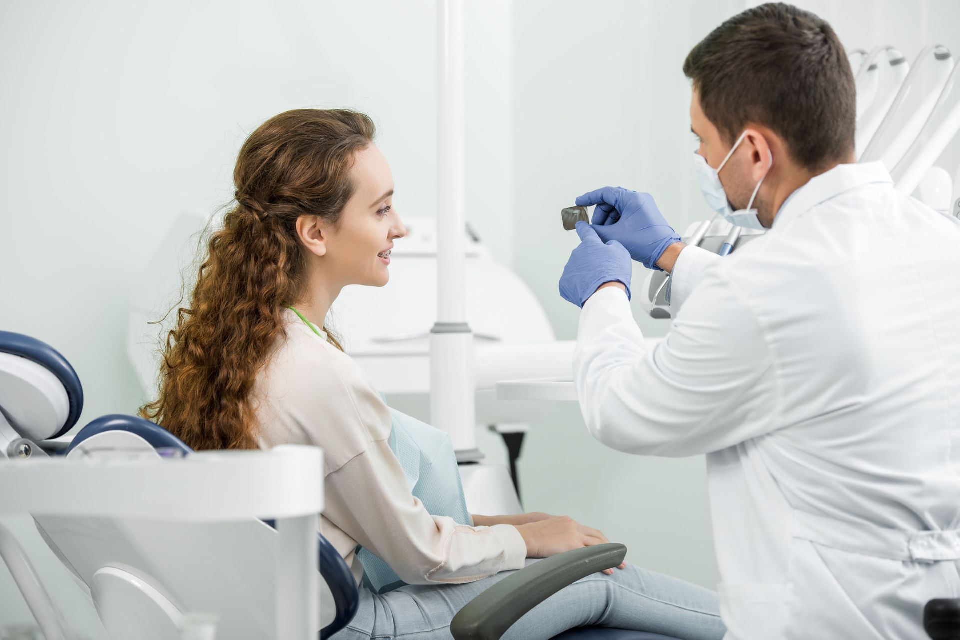 Dentista mostrando al paciente una herramienta dental en una oficina luminosa.