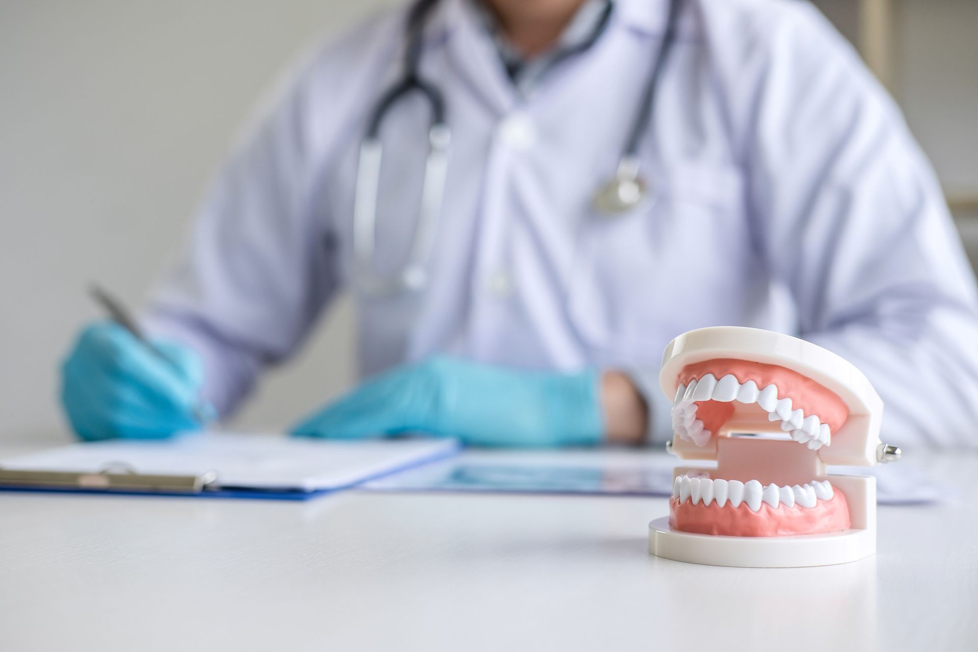 Médico con un estetoscopio escribiendo en un portapapeles; hay un modelo dental sobre el escritorio.