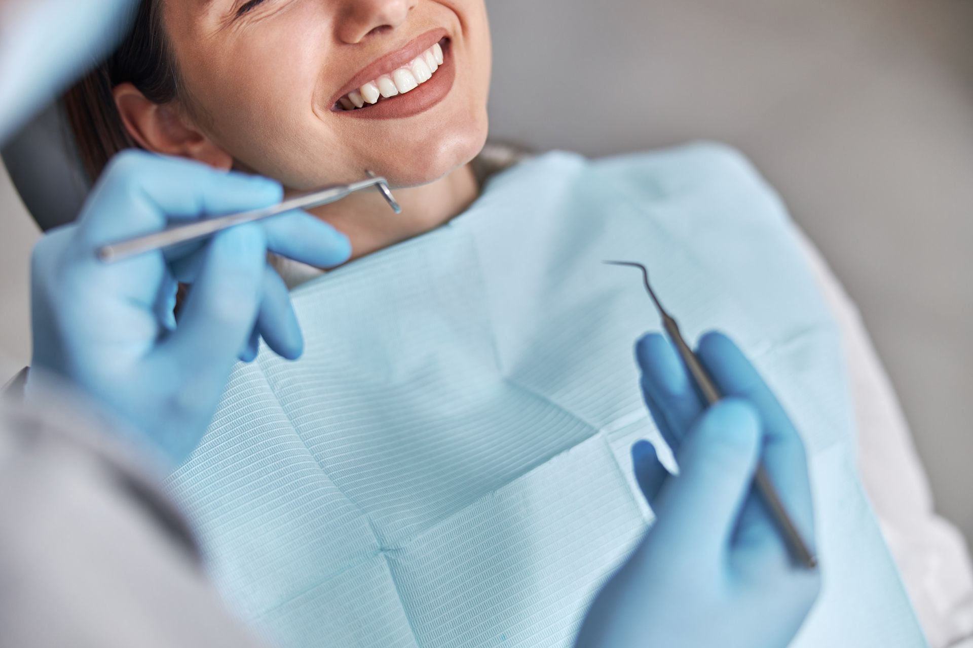 Dentista examina los dientes del paciente con herramientas dentales en una clínica; el paciente sonríe.