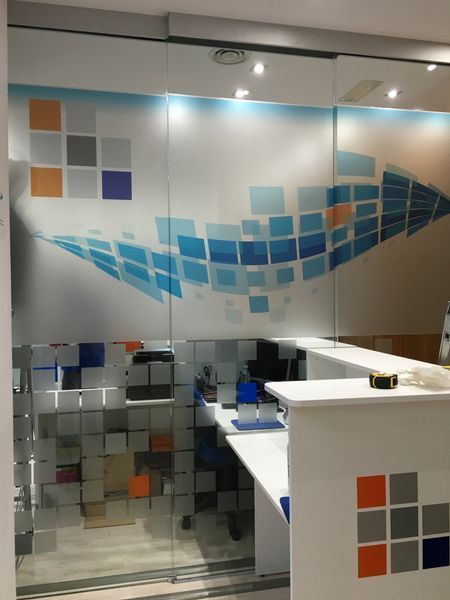 Paredes de oficina de vidrio y mostrador de recepción con diseño cuadrado azul, naranja y gris.