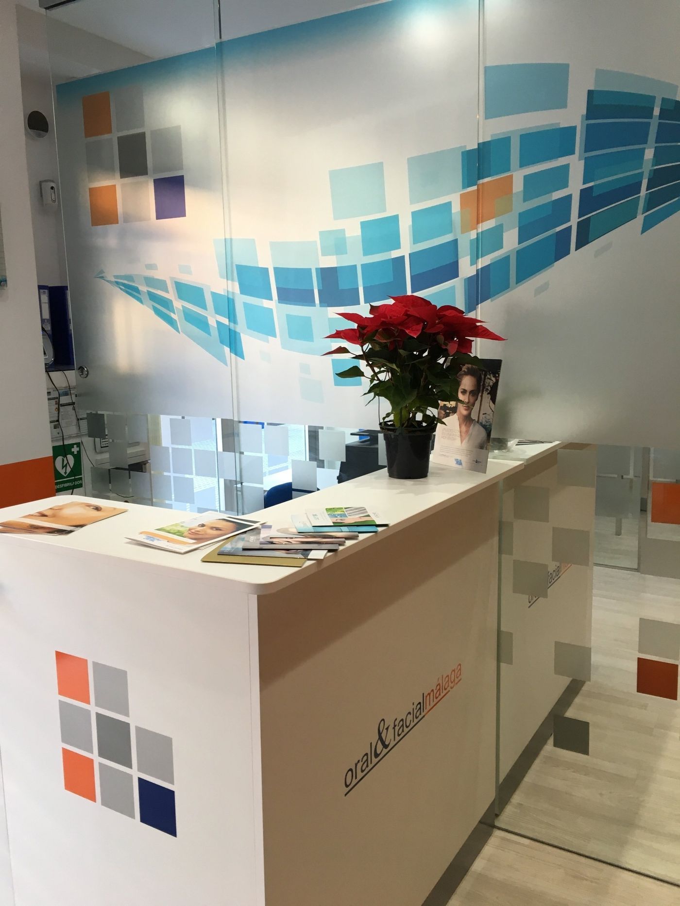 Mostrador de recepción con planta y logo frente a una pared de cuadrados.