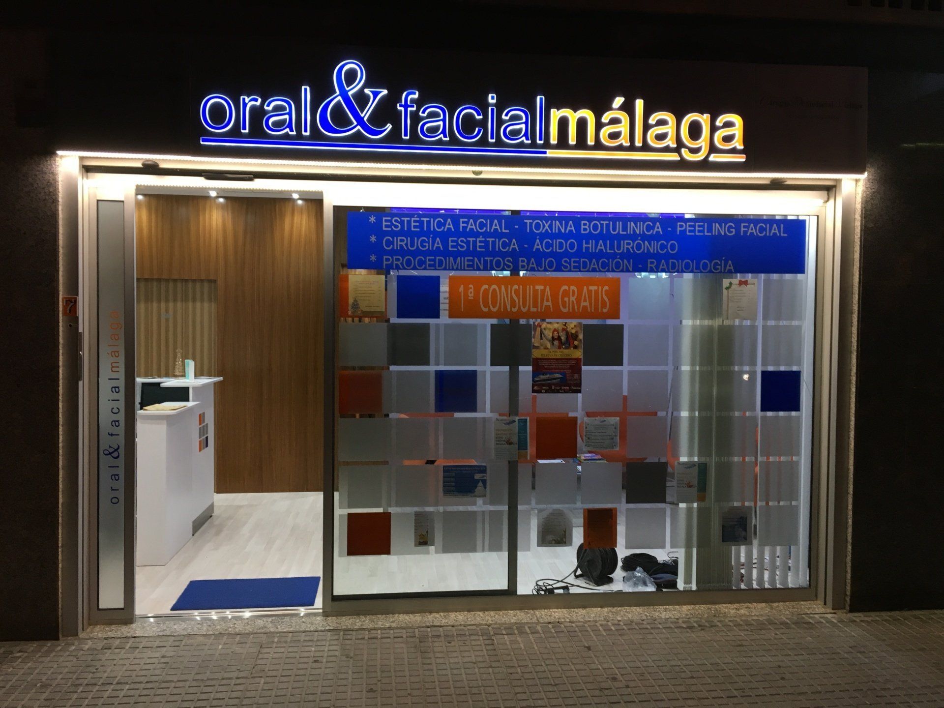 Exterior de la clínica Oral y Facial de Málaga de noche, cartel luminoso sobre la puerta.