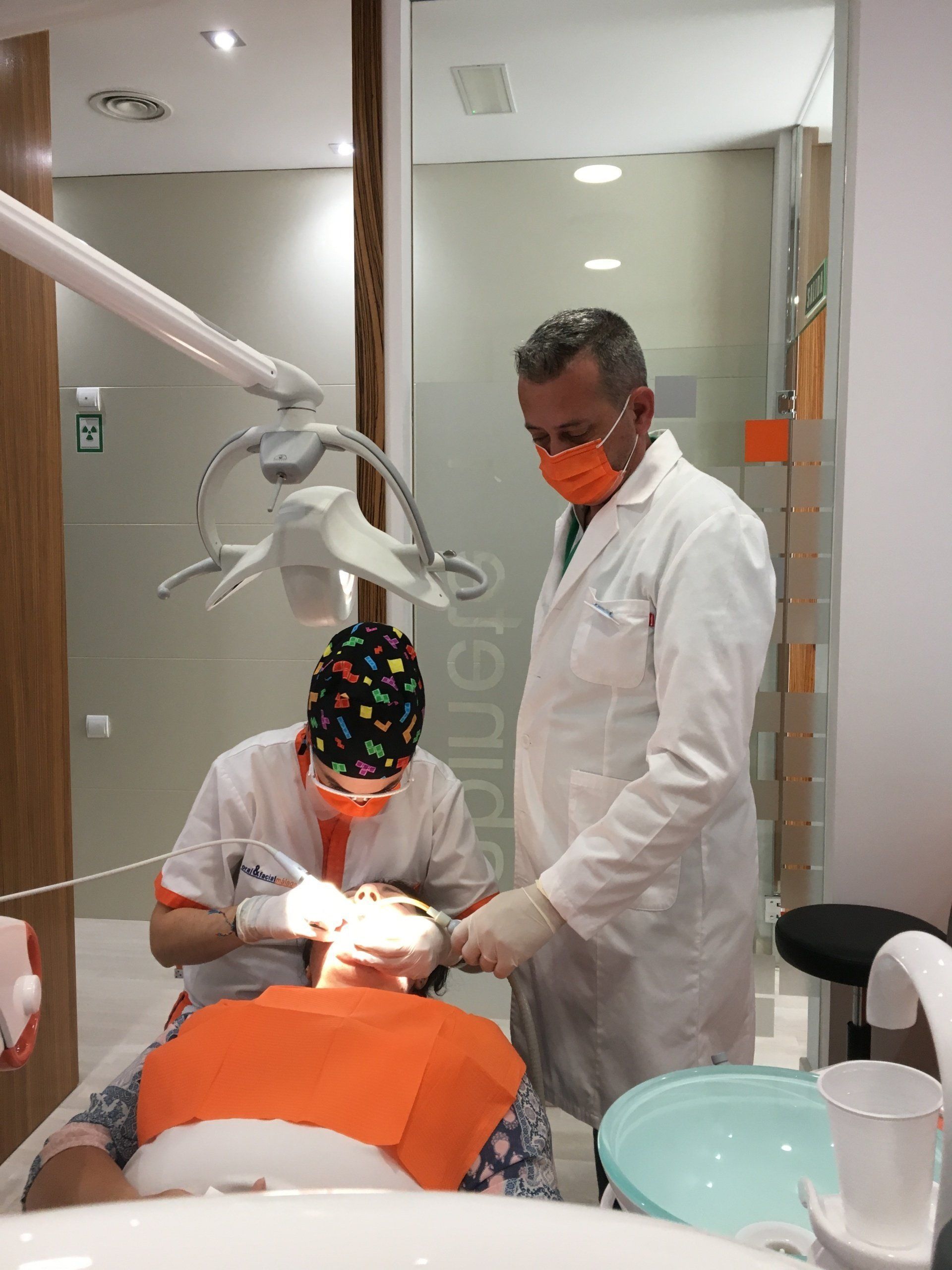 Dentista en una clínica examinando a un paciente. Los auxiliares llevan mascarillas y guantes.