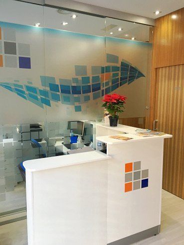 Mostrador de recepción blanco con logotipo colorido y fondo de vidrio esmerilado con diseño de flecha hacia arriba.