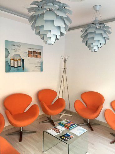 Sala de espera con sillas naranjas, mesa de cristal, luces decorativas y exhibición de productos.